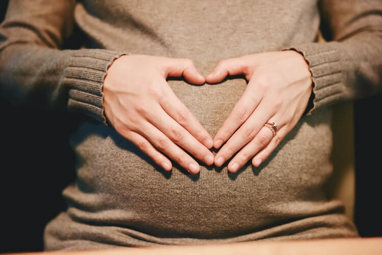 A pregnant person making a heart over their belly