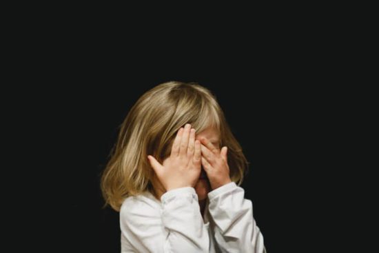 A young child covering her eyes